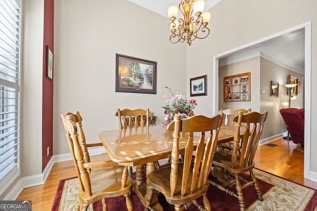 dining room featuring crown molding, light wood-type flooring, and a notable chandelier