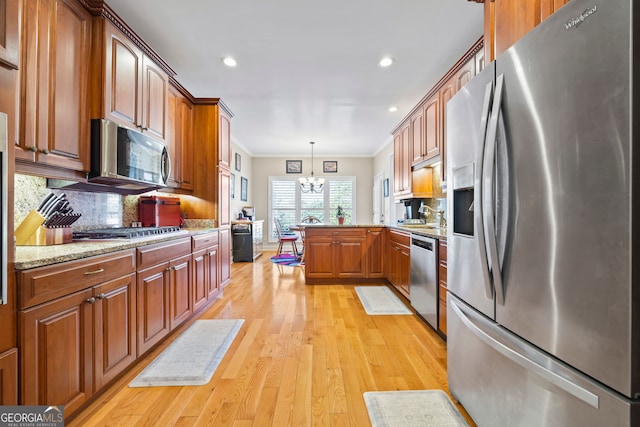 kitchen featuring tasteful backsplash, decorative light fixtures, a notable chandelier, stainless steel appliances, and light hardwood / wood-style floors