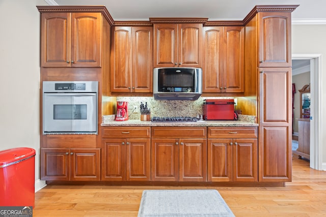 kitchen with tasteful backsplash, light stone counters, light wood-type flooring, ornamental molding, and stainless steel appliances