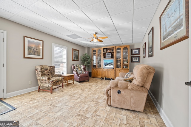 living area with a paneled ceiling and ceiling fan