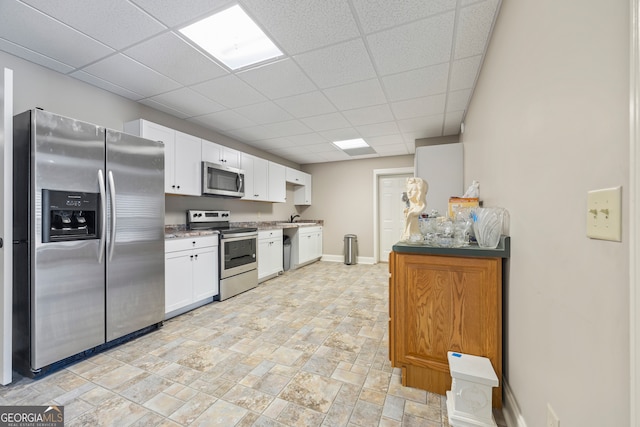 kitchen with appliances with stainless steel finishes, sink, a drop ceiling, and white cabinets