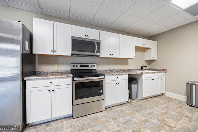 kitchen featuring sink, a paneled ceiling, appliances with stainless steel finishes, light stone countertops, and white cabinets