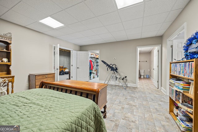 bedroom with a walk in closet, ensuite bathroom, a closet, and a drop ceiling