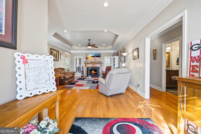 living room with ceiling fan, wood-type flooring, a tray ceiling, and ornamental molding