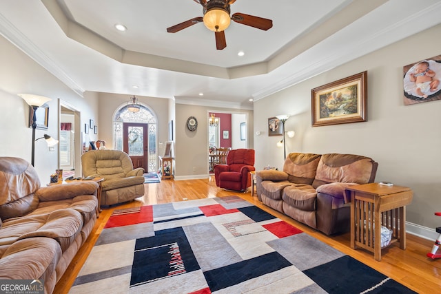 living room with crown molding, ceiling fan, a tray ceiling, and light hardwood / wood-style floors