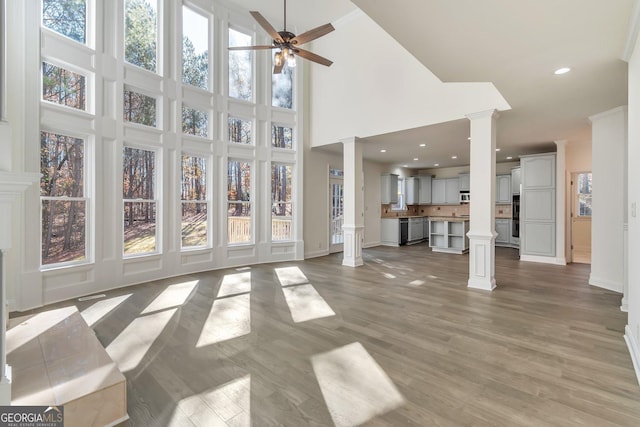 unfurnished living room featuring ceiling fan, a towering ceiling, hardwood / wood-style flooring, and ornate columns