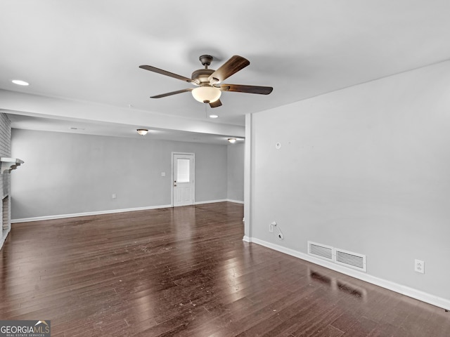 empty room with dark wood-type flooring, ceiling fan, and a brick fireplace