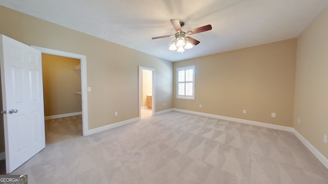 unfurnished bedroom featuring ensuite bathroom, a walk in closet, light colored carpet, ceiling fan, and a closet