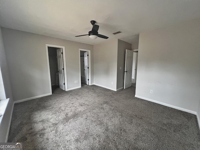 unfurnished bedroom with ensuite bathroom, dark colored carpet, a spacious closet, ceiling fan, and a closet