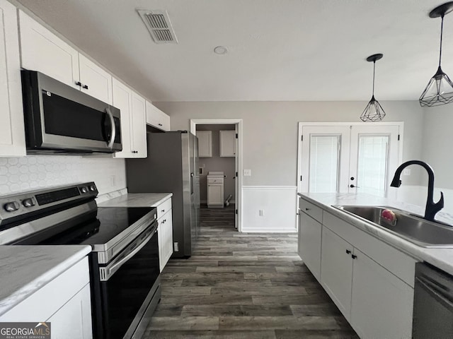 kitchen with appliances with stainless steel finishes, pendant lighting, white cabinetry, sink, and decorative backsplash