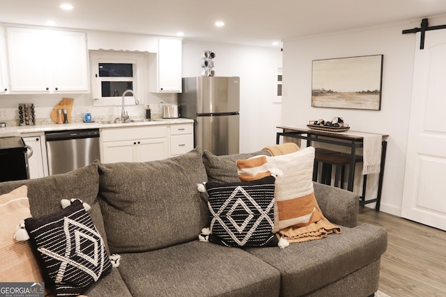 kitchen featuring sink, white cabinetry, light hardwood / wood-style flooring, stainless steel appliances, and a barn door