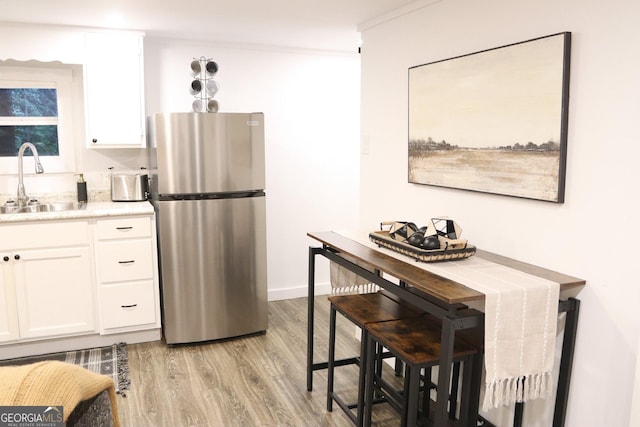 kitchen with white cabinetry, sink, stainless steel fridge, ornamental molding, and light wood-type flooring