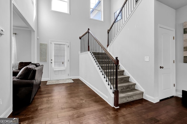 foyer entrance with dark wood-style floors, stairway, baseboards, and a towering ceiling