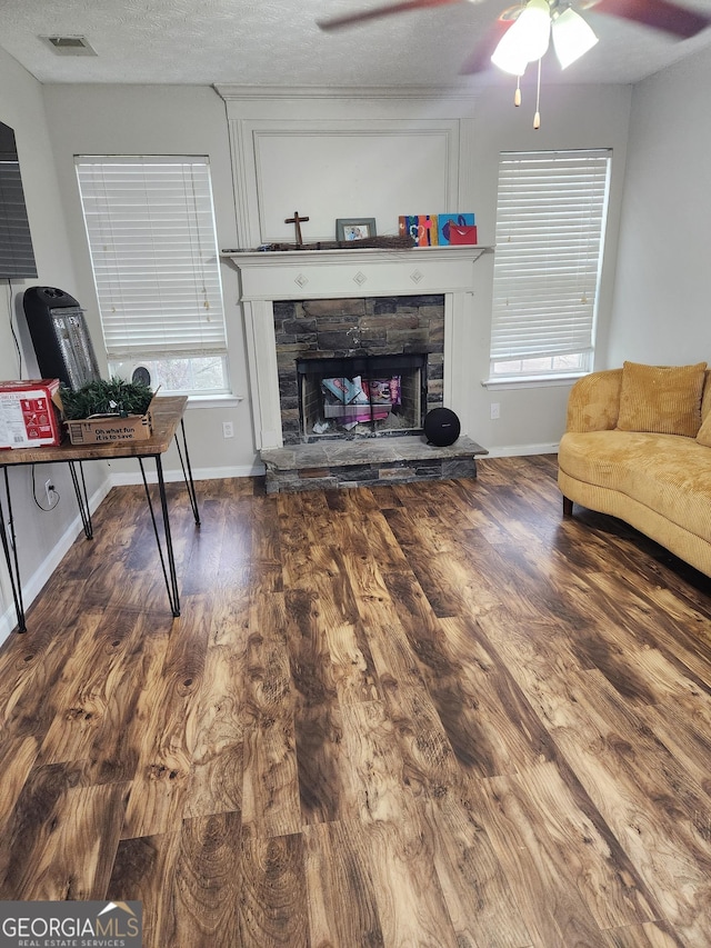 living room with ceiling fan, a fireplace, dark hardwood / wood-style floors, and a textured ceiling