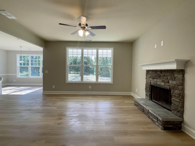 unfurnished living room featuring ceiling fan, a stone fireplace, and light hardwood / wood-style floors