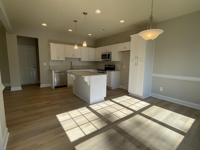 kitchen featuring light hardwood / wood-style flooring, appliances with stainless steel finishes, a center island, white cabinets, and decorative backsplash