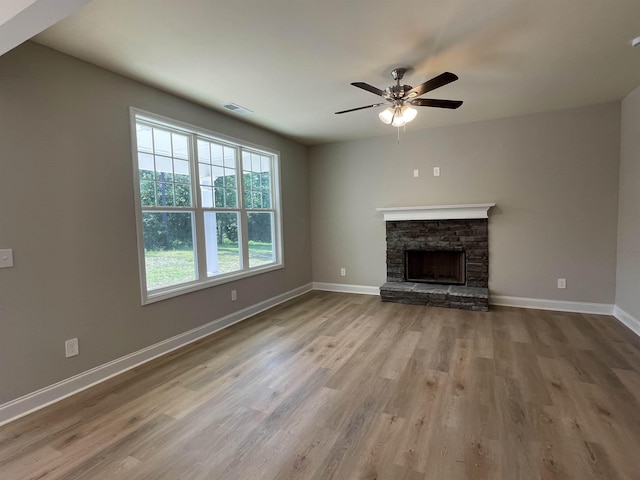 unfurnished living room with ceiling fan, a stone fireplace, and light hardwood / wood-style floors