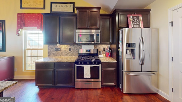 kitchen featuring light stone counters, dark brown cabinets, stainless steel appliances, and tasteful backsplash