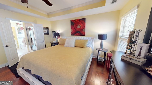 bedroom with crown molding, a tray ceiling, dark wood-type flooring, and ceiling fan