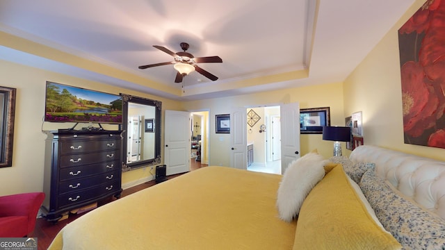 bedroom with ensuite bath, wood-type flooring, ornamental molding, a raised ceiling, and ceiling fan