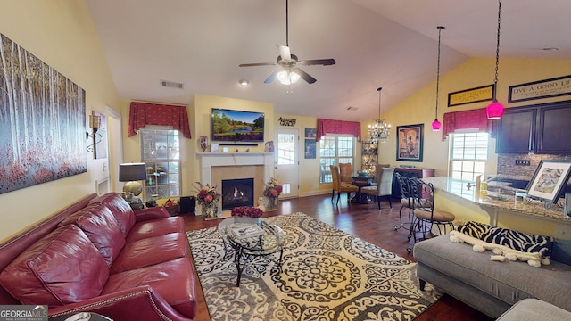 living room featuring dark wood-type flooring, high vaulted ceiling, a tiled fireplace, and ceiling fan with notable chandelier