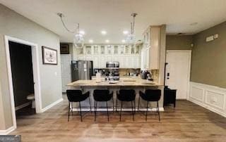 kitchen with hanging light fixtures, light wood-type flooring, appliances with stainless steel finishes, a kitchen breakfast bar, and kitchen peninsula