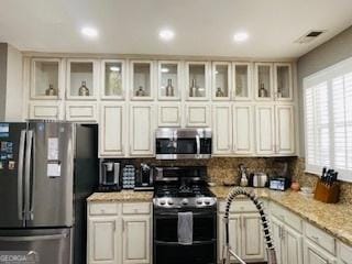 kitchen featuring appliances with stainless steel finishes, light stone countertops, and cream cabinetry