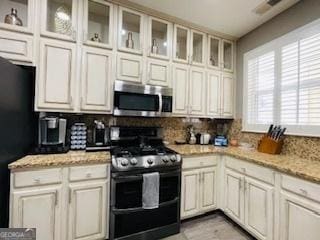 kitchen featuring black refrigerator, double oven range, tasteful backsplash, and light stone countertops