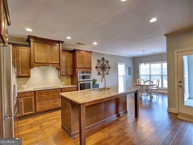 kitchen with hanging light fixtures, wood-type flooring, appliances with stainless steel finishes, and ornamental molding