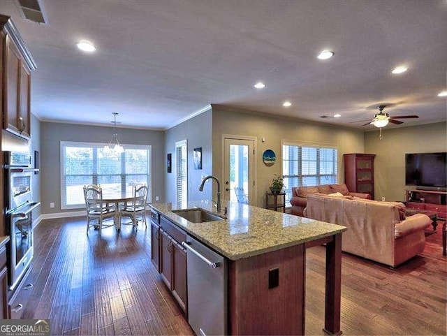 kitchen featuring decorative light fixtures, dishwasher, sink, ornamental molding, and a center island with sink