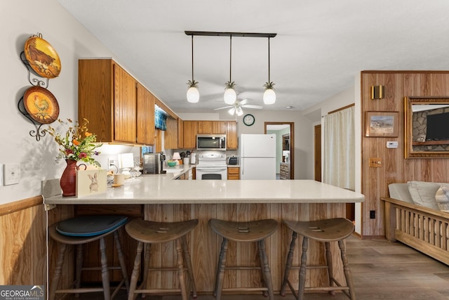 kitchen with wood walls, hanging light fixtures, dark hardwood / wood-style floors, kitchen peninsula, and white appliances