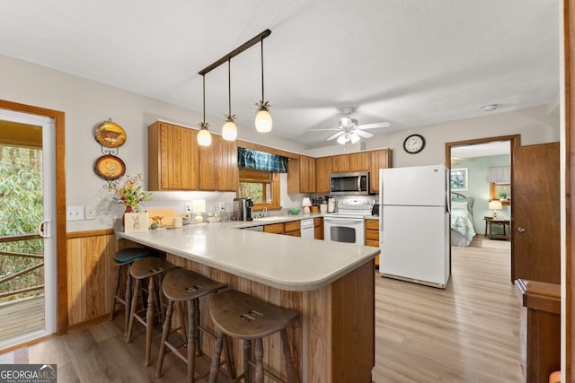 kitchen with white appliances, pendant lighting, kitchen peninsula, and light wood-type flooring