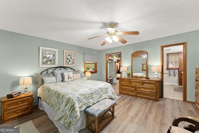 bedroom featuring ceiling fan, ensuite bathroom, a textured ceiling, and light wood-type flooring