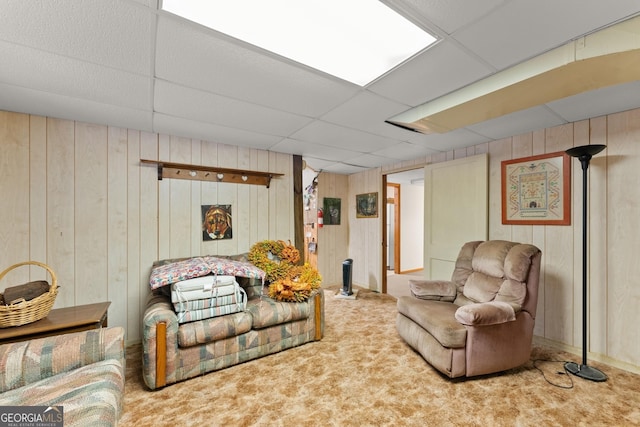 living room featuring a drop ceiling, wood walls, and carpet flooring