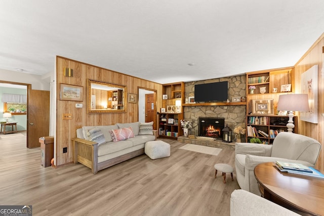 living room featuring a fireplace, built in features, wooden walls, and light wood-type flooring