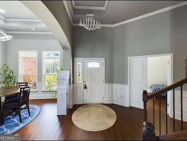 foyer entrance with crown molding, an inviting chandelier, a high ceiling, a tray ceiling, and dark hardwood / wood-style flooring