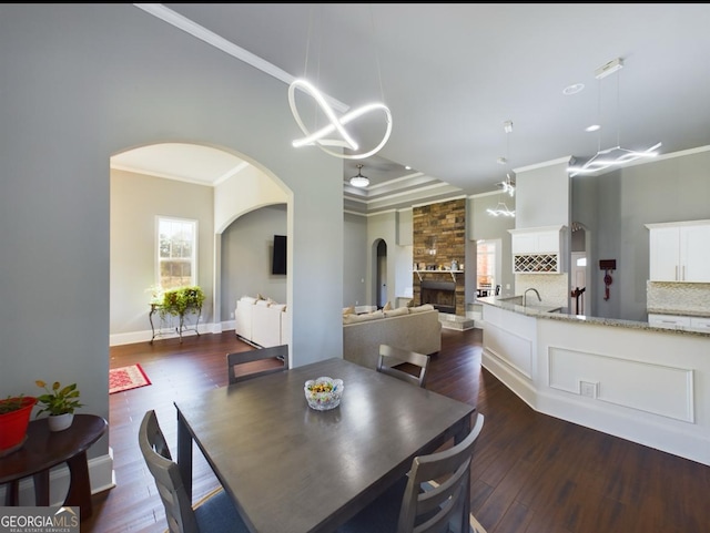 dining area featuring dark wood-type flooring, ornamental molding, a stone fireplace, and a notable chandelier