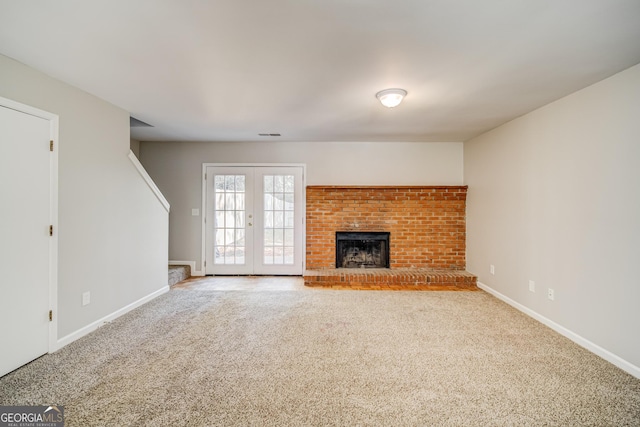 unfurnished living room with a brick fireplace, french doors, and carpet flooring