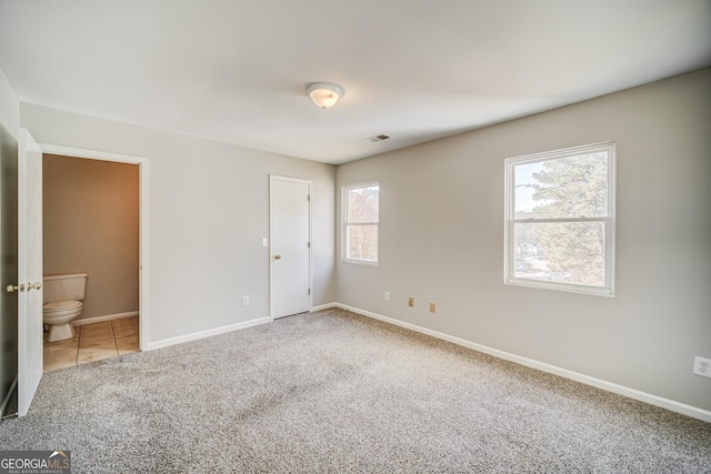 unfurnished bedroom featuring multiple windows, connected bathroom, and carpet flooring