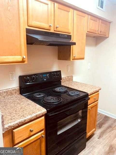 kitchen featuring black range with electric stovetop, light hardwood / wood-style floors, and light stone countertops