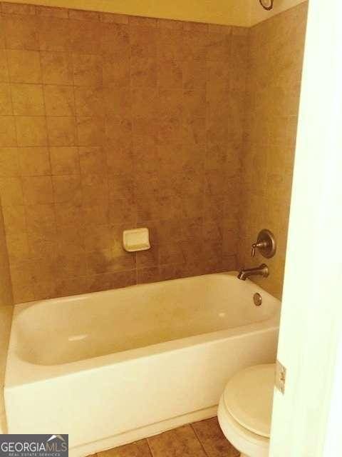 bathroom with tiled shower / bath, toilet, and tile patterned flooring