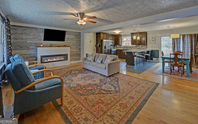 living room with ceiling fan, a textured ceiling, and light wood-type flooring