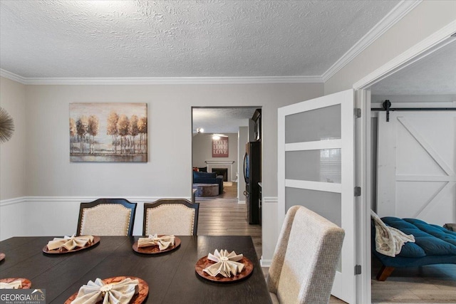 dining space featuring hardwood / wood-style floors, crown molding, a barn door, and a textured ceiling