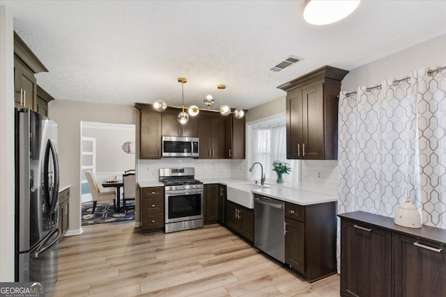 kitchen featuring appliances with stainless steel finishes, decorative light fixtures, sink, decorative backsplash, and light wood-type flooring