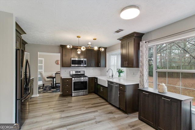 kitchen featuring sink, tasteful backsplash, decorative light fixtures, light hardwood / wood-style flooring, and appliances with stainless steel finishes