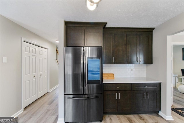 kitchen featuring decorative backsplash, dark brown cabinets, stainless steel fridge, and light hardwood / wood-style flooring