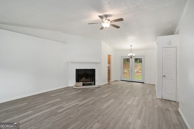 unfurnished living room featuring french doors, ceiling fan with notable chandelier, light hardwood / wood-style flooring, and a textured ceiling