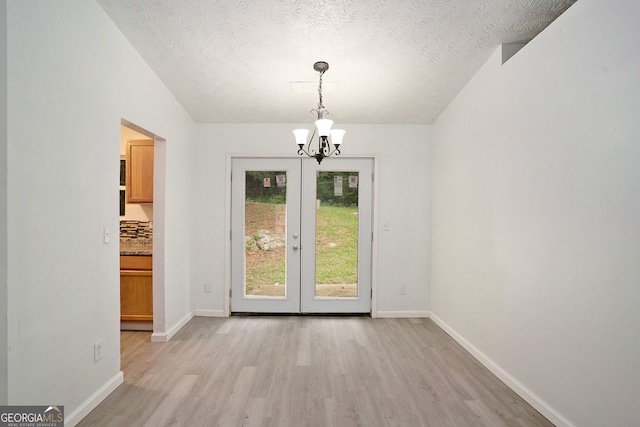 unfurnished dining area with an inviting chandelier, french doors, light hardwood / wood-style flooring, and a textured ceiling