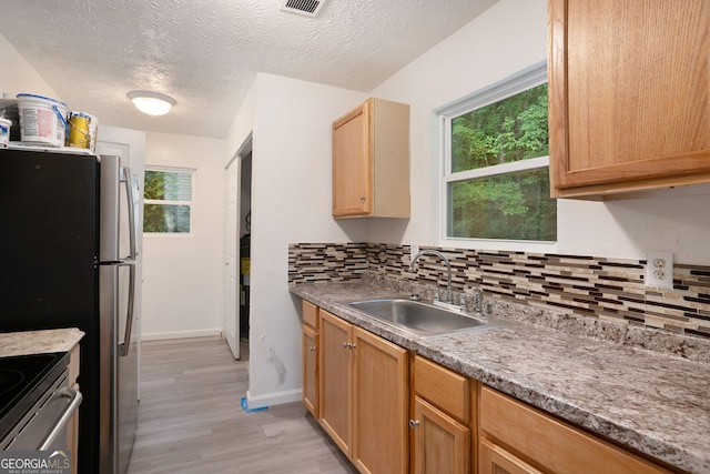 kitchen with sink, a textured ceiling, appliances with stainless steel finishes, light hardwood / wood-style floors, and decorative backsplash