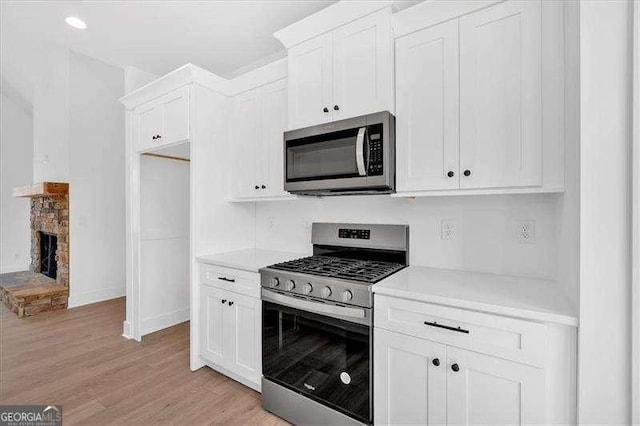 kitchen featuring a stone fireplace, stainless steel appliances, light hardwood / wood-style floors, and white cabinets